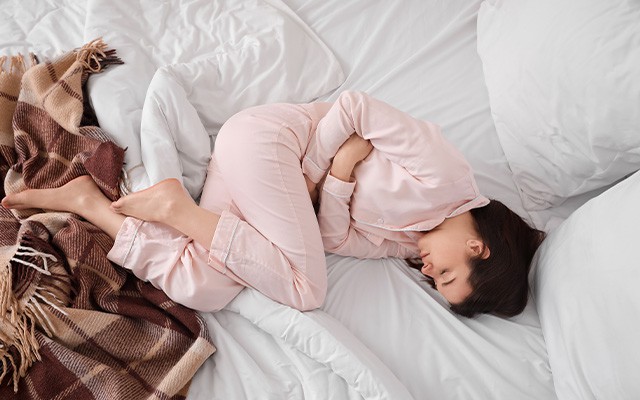 Frau mit PMS liegt zusammengerollt im Bett